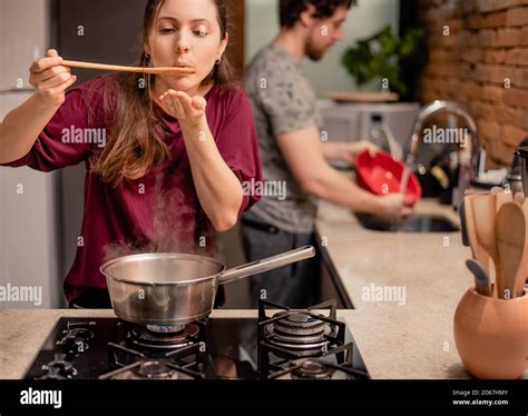 Woman Tasting Food From The Pan And Man Washing Dishes Stock Photo Alamy