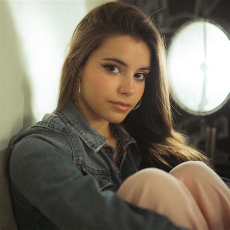 A Woman With Long Hair Sitting In Front Of A Wall And Looking At The Camera