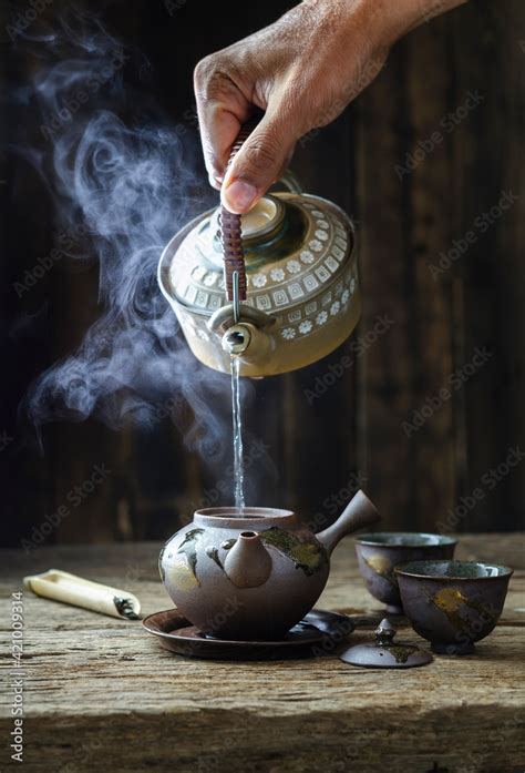 Pouring Hot Water From A Pot Into Teapot Steam Is Over The Teapot There Is Tea In The Bamboo