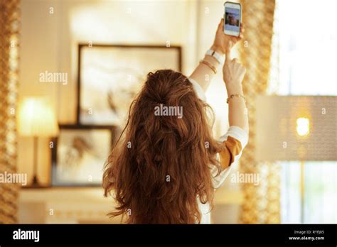 Seen From Behind Fit Housewife With Long Brunette Hair At Modern Home Trying To Get Better Wifi