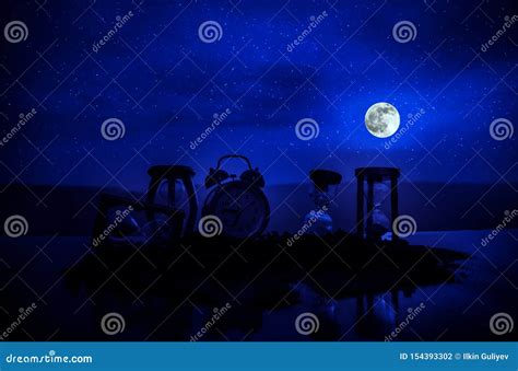 Time Concept With A Hourglass At Night With Moon Or Sand Passing Through The Glass Bulbs Of An