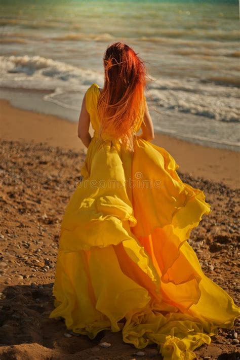 Beautiful Girl Walks Along The Sandy Beach In A Yellow Dress Stock