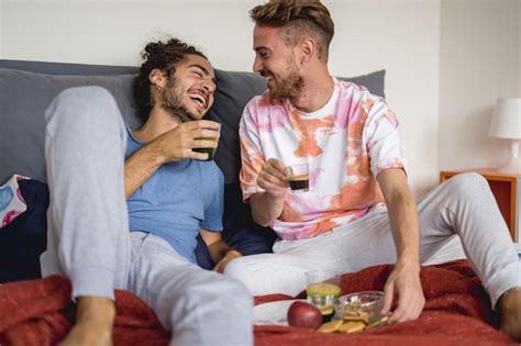 Jovem casal gay na cama tomando café da manhã amantes felizes bebendo café e se divertindo pela