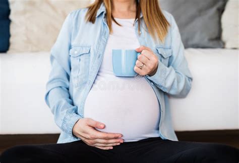 Pregnant Woman Sitting On Floor In Front Of Sofa Drinking Herbal Tea