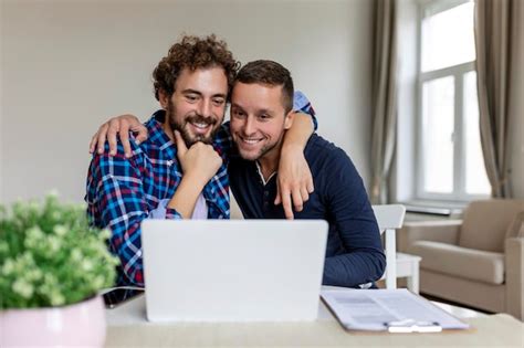Lindo casal gay rindo juntos enquanto está sentado em sua sala de estar em casa dois românticos
