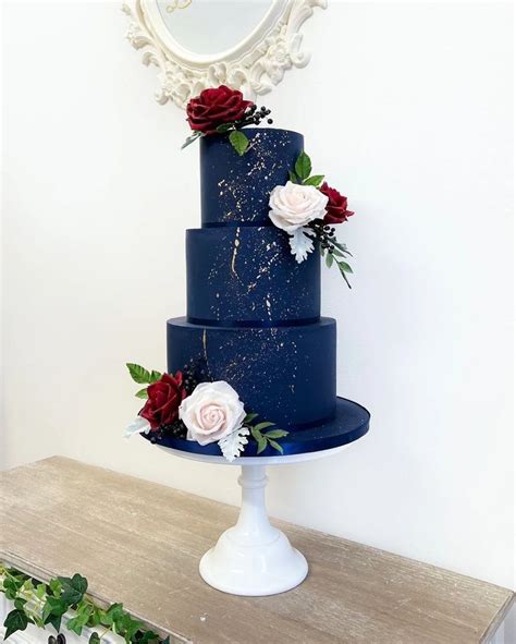 A Three Tiered Blue Cake With Red And White Flowers On The Top Is