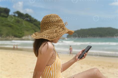 joven mujer hermosa en bikini escuchando música y usando un smartphone en la playa verano