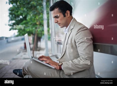 Businessman Sitting On A Bench At Bus Stop And Working On A Laptop