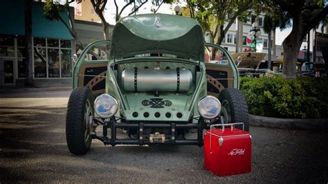 An Old Green Car Parked In Front Of A Building Next To A Red Cooler Box