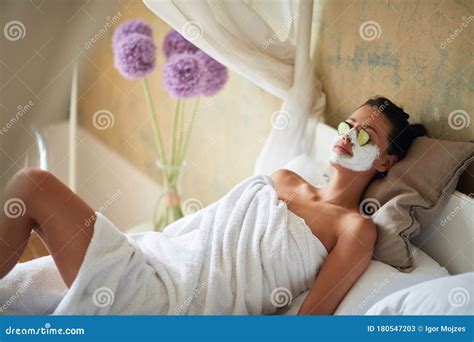 Woman And Facial Clay Mask On Face And Cucumber On Eyes Relaxing In Bed