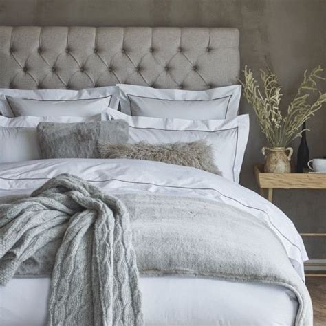 A Bed With White Linens And Pillows In A Gray Room Next To A Wooden Table