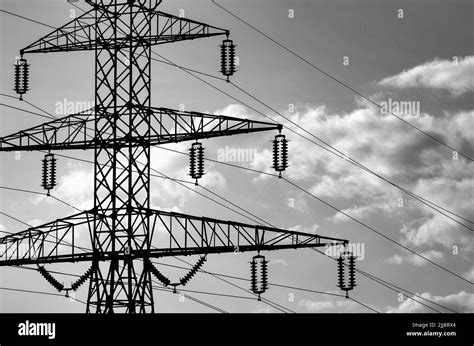 A Closeup Of A High Voltage Pylon Under A Cloudy Sky In Greyscale Stock