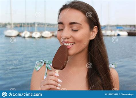 Beautiful Young Woman Eating Ice Cream Glazed In Chocolate Near River