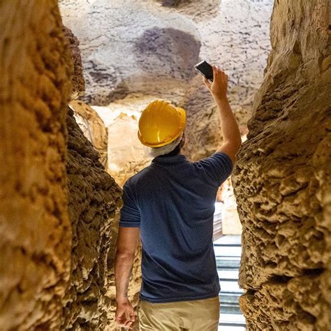 A Man Wearing A Hard Hat And Holding A Cell Phone Up To The Ceiling In