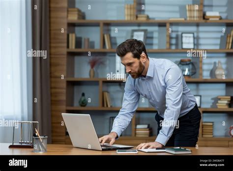Focused Mature Businessman Reviewing Documents At His Laptop In A Well Organized Modern Home