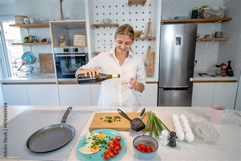 Beautiful Blonde Woman Cooking In A Modern Equipped Kitchen Preparing Fried Eggs And Pouring