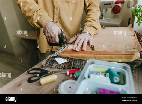 Man securing fabric from old clothes on chair with stapler at home ...