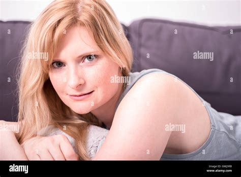 Beautiful Blonde Woman Is Smiling And Relaxing On Gray Couch Stock Photo Alamy