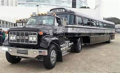 An Old Black Bus Is Parked In Front Of Some Other Buses And People Are