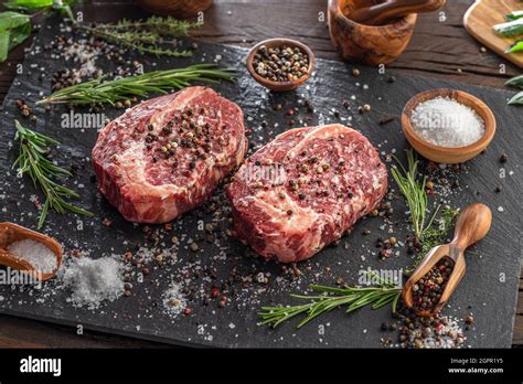 Raw Ribeye Steaks With Salt And Herbs On Grey Board Top View Stock