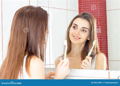 Joyful Young Girl Stands In Front Of A Mirror And Holds In Her Hand The