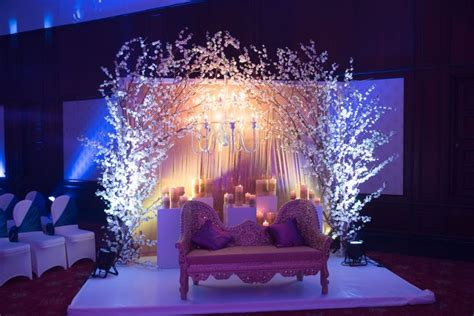 A Stage Set Up For A Wedding With Candles And Flowers On The Back Wall Surrounded By Chairs