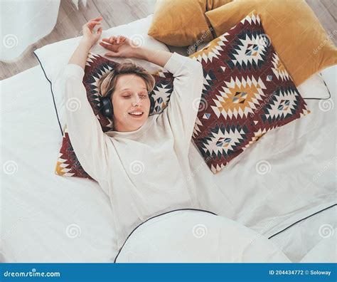 Smiling Young Female Lying On Cozy Bed Dressed Pajamas Listening To