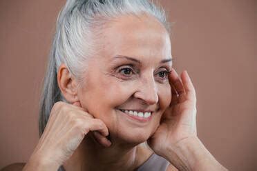 Portrait Of Naked Senior Woman With Grey Hair In Front Of Brown Background Stock Photo