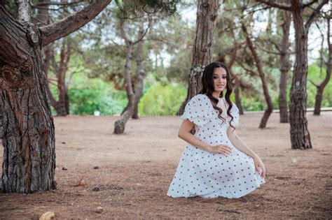Beautiful Slim Brunette Woman In Summer White Dress Walking Among Trees In Park Stock Image