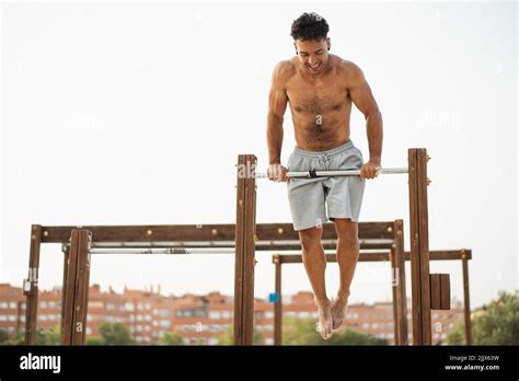 Low Angle Of Muscular Hispanic Ethnic Male Athlete With Naked Torso Doing Bar Muscle Up Exercise