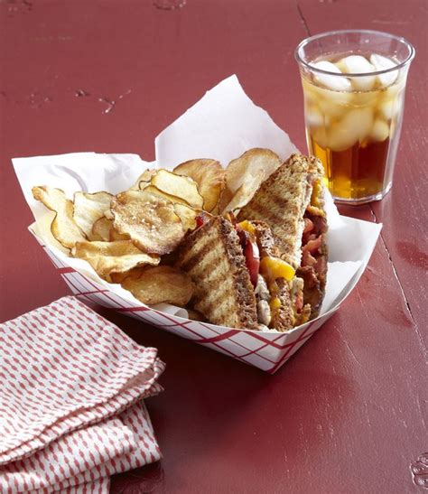 A Basket Filled With Sandwiches And Chips Next To A Glass Of Soda On