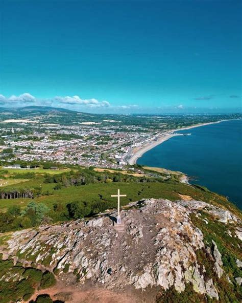 A Cross On Top Of A Hill Overlooking The Ocean And Town Below It With