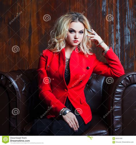 Junge Und Attraktive Blonde Frau In Der Roten Jacke Sitzt Im Ledersessel Rostige Wand Des