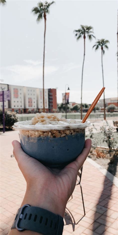 A Person Holding Up A Bowl Of Food In Front Of Palm Trees