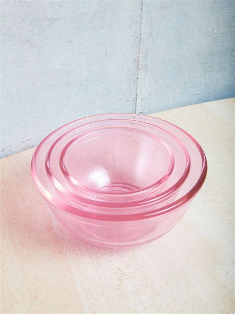 A Pink Glass Bowl Sitting On Top Of A Wooden Table Next To A White Wall