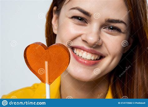 Cheerful Pretty Woman Licking Heart Shaped Lollipop Close Up Studio