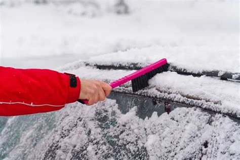 Man Cleaning Snow From Car Windshield With Brush In Winter Morning