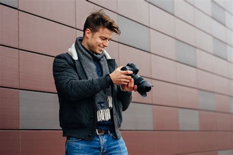 Guapo joven fotógrafo de pie con la cámara al aire libre contra el