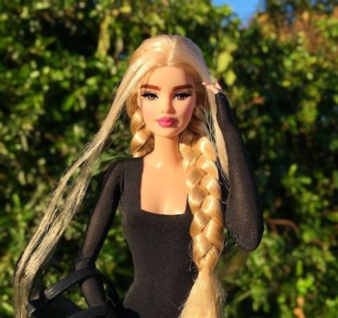 A Barbie Doll With Long Blonde Hair Wearing A Black Dress And Holding A