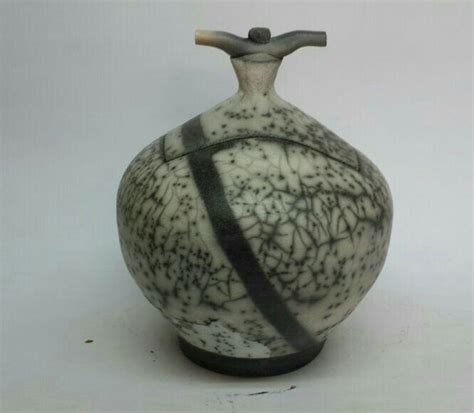 A Black And White Vase With Lines Painted On The Side Sitting Against