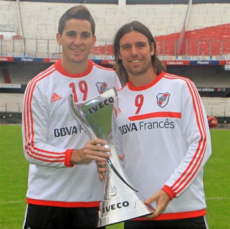 Two Men Standing Next To Each Other On A Field Holding Up A Silver