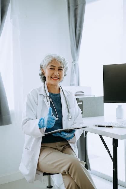 Premium Photo Confident Mature Asian Female Doctor In White Medical Uniform Sit At Desk