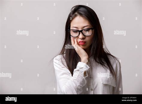 Portrait Of Sad Asian Woman In Glasses And White Shirt On Gray