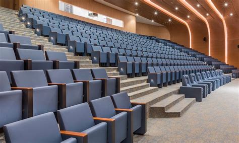 An Empty Auditorium With Rows Of Blue Chairs And Steps Leading Up To