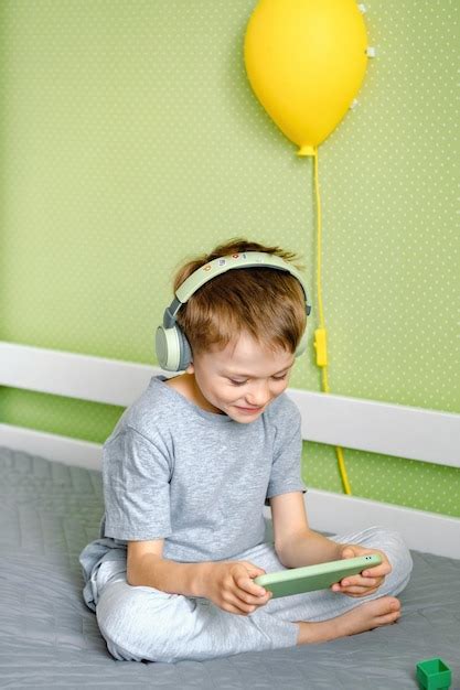 Un Ni O En Edad Preescolar Sentado En La Cama Usando Auriculares