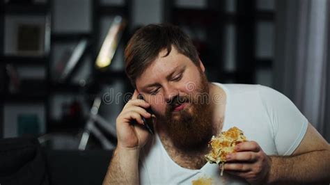 Dirty Fat Bearded Man Talks On The Smartphone Eating A Burger And