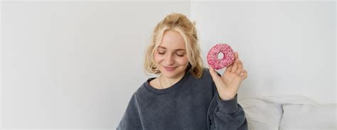 Portrait d une jolie fille blonde tenant un donut rose avec des éclaboussures sur le dessus