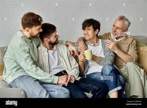A Gay Couple Sits With Parents On A Couch At Home Sharing A Warm And Intimate Moment Stock