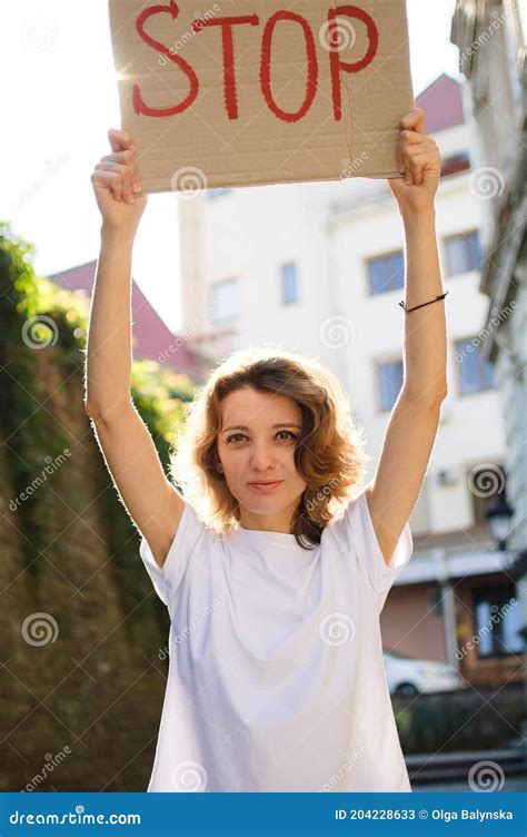 Young Protesting Woman In White Shirt And Jeans Holds Protest Sign