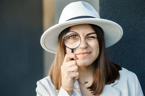 Curious Young Woman In White Hat Looking Through A Magnifying Glass